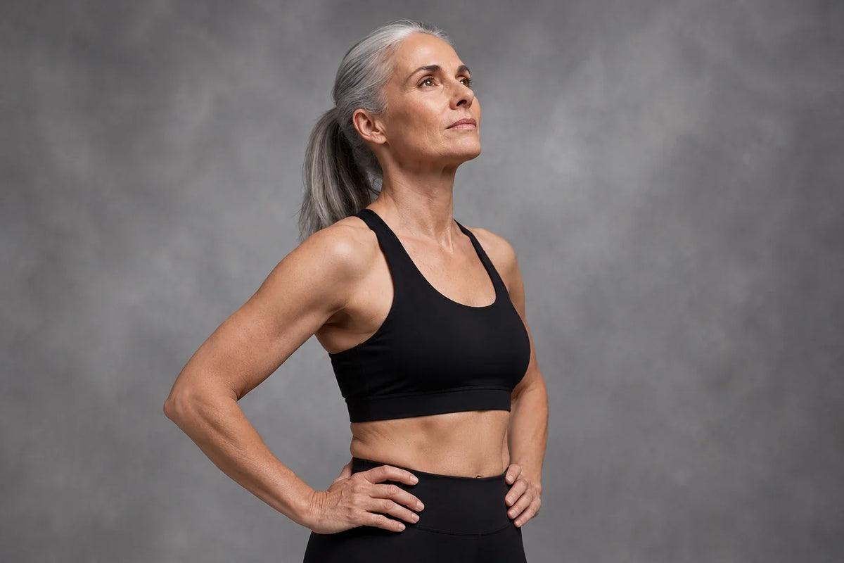 Silver-haired woman in black training clothes against a grey background